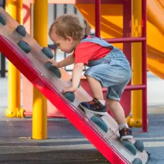 Een peuter klimt op een speeltoestel. Dit is een voorbeeld van hoe kinderen spelenderwijs leren, wat betekent bso: buiten school opvang, waar ze dit soort activiteiten kunnen doen.