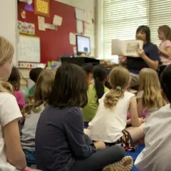 Kinderen zitten aandachtig te luisteren naar de juf die voorleest. Een mooi voorbeeld van leren van elkaar in de klas.