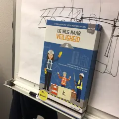 Doos van het spel "De Weg Naar Veiligheid" met bouwfiguren. Het spel moedigt aan om nog veiliger te werken, zodat iedereen veilig gespeld wordt.