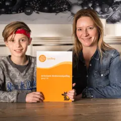 Moeder en zoon houden een oefenboek spelling vast. Vind je het leuk om te leren spellen?