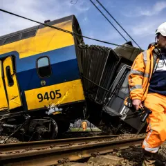 Een ontspoorde trein, nummer 9405, ligt scheef op het spoor. Een man in oranje werkkleding inspecteert de schade, de wagons lijken per ongeluk aan elkaar of los te zijn geraakt.