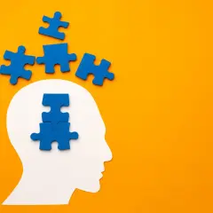 Blauwe puzzelstukjes vallen uit een witte hoofdvorm, sommigen boven, anderen in het hoofd. Het symboliseert het proces van het oplossen van gedachten, zoals bij pdd nos engels.