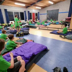 Kinderen van kamp groep 8 liggen op slaapzakken in een gymzaal, klaar voor een nacht vol avontuur.