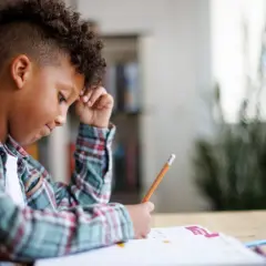 Jongen met krullend haar verdiept in zijn huiswerk, een potlood in zijn hand, navigeert door de wereld van getallen.