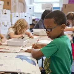 Kinderen met potloden aan het werk, sommigen met een boek over de 'Blackbird'. Een jongen met bril, avi 8 leesniveau, tekent aandachtig.