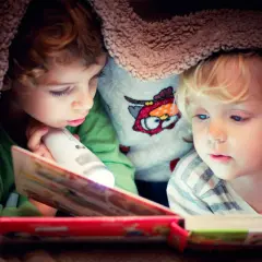 Twee kinderen lezen onder een deken met een zaklamp. Een verhaal dat de woordenschat van groep 8 verrijkt.