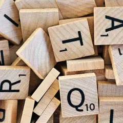 Houten lettertegels, zoals gebruikt bij moderne vreemde talen, liggen door elkaar. Letters als A, T, R, Q en N zijn zichtbaar.