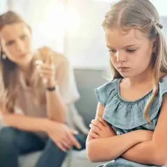 Een meisje met gekruiste armen toont duidelijk oppositioneel gedrag, terwijl haar moeder op de achtergrond met haar vinger waarschuwt.