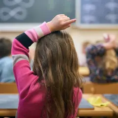 Een meisje met dyscalculie op de middelbare school steekt haar vinger op, hopend op hulp bij de sommen op het bord.