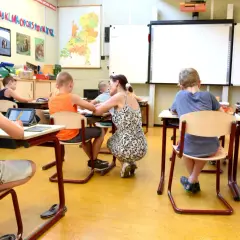 Een lerares geeft individuele aandacht aan leerlingen in een klaslokaal, wat de kern vormt van traumasensitief onderwijs.