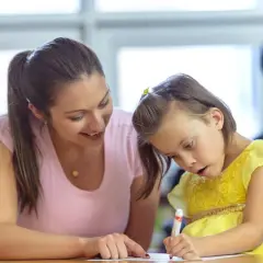 Een vrouw helpt een meisje met autisme met haar huiswerk. Ze probeert haar zin te doordrijven en te motiveren.