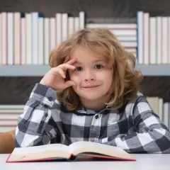 Een jongen met een boek, omringd door boeken. Zijn blik suggereert diepe gedachten, mogelijk over dcd en hoogbegaafdheid.