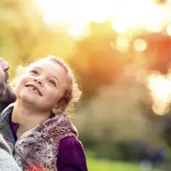 Vader en dochter kijken elkaar liefdevol aan in het gouden zonlicht. Hun band is onbreekbaar, een geschenk dat pdd-nos erfelijk is.