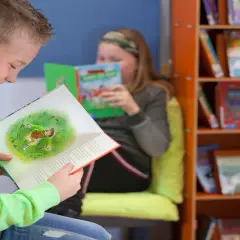 Jongen in groen shirt geniet van een boek met een illustratie. Achter hem leest een meisje. Dit is een typisch beeld van lezen groep 4.