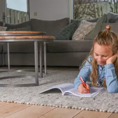 Een meisje ligt op een kleed en maakt huiswerk, ze oefent met breuken delen.