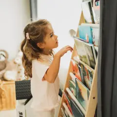 Een meisje met blond haar kijkt aandachtig naar de boekenplank, klaar om een nieuw avontuur te ontdekken. Ze houdt van lezen, kinderen.
