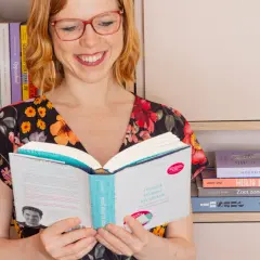 Vrouw met bril leest boek, "nooit meer te druk". Ze is omringd door boeken, wat een **betrekkelijk voornaamwoord** is voor haar passie.