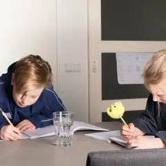 Twee kinderen maken huiswerk aan tafel. De jongen schrijft met een potlood, de meid met een leuke gele pen. Ze oefenen met delen met kommagetallen.