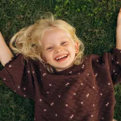 Lachend meisje met blonde krullen ligt op gras. Ze geniet van de rust, een moment van kalmte bij onderprikkeling ADHD.