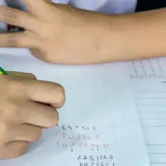 Een leerling uit groep 8 is bezig met rekenen. De leerling schrijft cijfers op papier, met een potlood.