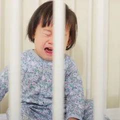 Een huilend kind in een ledikant, met gesloten ogen en open mond. Het kind draagt een pyjama met bloemenprint. Dit kan duiden op sensorische overprikkeling, zoals bij hoofd bonken autisme.
