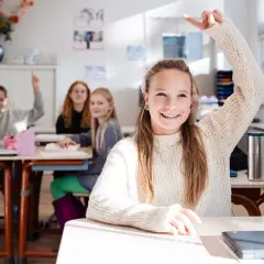 Vrolijke leerlingen steken hun hand op in een klaslokaal. De sfeer is positief, ondanks de mogelijke particulier onderwijs kosten.