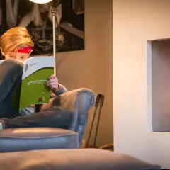 Kind met rood bandje leest een oefenboek rekenen bij de haard.