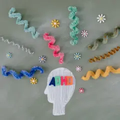 Kleurrijke linten en bloemen omringen een hoofdprofiel met de letters "ADHD". Dit symboliseert de zoektocht naar een kind behandeling.