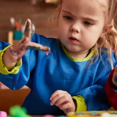 Een peuter met verf aan haar handen, die geconcentreerd aan het schilderen is. Dit is een mooi voorbeeld van cognitieve ontwikkeling peuter door creatief spel.