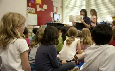 Kinderen zitten aandachtig te luisteren naar de juf die voorleest. Een mooi voorbeeld van leren van elkaar in de klas.
