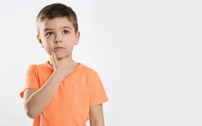 Jongetje met oranje shirt denkt diep na, misschien een beetje traag van begrip, met zijn vinger op zijn kin.