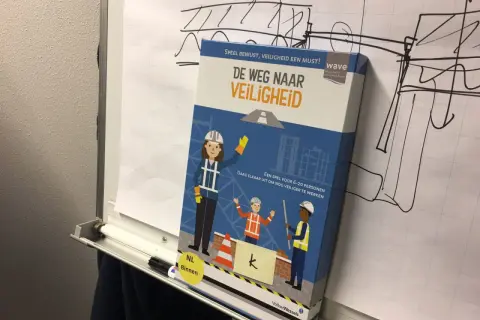 Doos van het spel "De Weg Naar Veiligheid" met bouwfiguren. Het spel moedigt aan om nog veiliger te werken, zodat iedereen veilig gespeld wordt.
