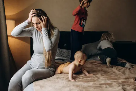 Een moeder met handen in haar hoofd, overdonderd door de drukte van haar kinderen. Een dag met adhd en autisme kan intens zijn.