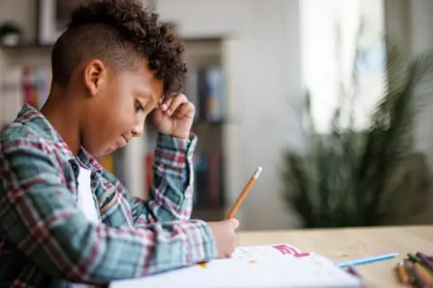Jongen met krullend haar verdiept in zijn huiswerk, een potlood in zijn hand, navigeert door de wereld van getallen.