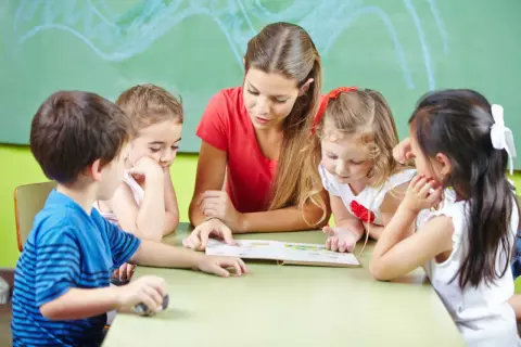 Jonge kinderen luisteren aandachtig naar de juf die voorleest. De leeftijdsgrens basisschool 1 januari is bereikt voor sommigen.