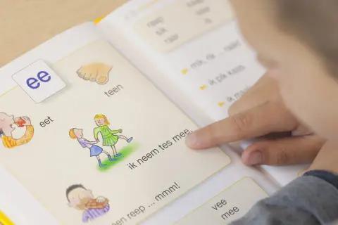 Kind leert woordenschat groep 3 uit een boekje. De letter 'ee' staat centraal, met illustraties van eten en spelen.