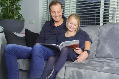 Vader en dochter lezen samen een rekenboek. De tafels flitsen door hun hoofd terwijl ze oefenen.
