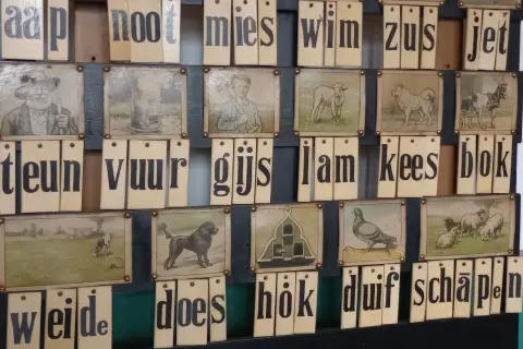 Oude letterkaarten met afbeeldingen, die samen Nederlandse uitdrukkingen vormen zoals 'aap, noot, mies'.