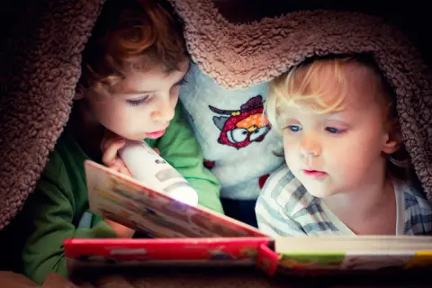 Twee kinderen lezen onder een deken met een zaklamp. Een verhaal dat de woordenschat van groep 8 verrijkt.