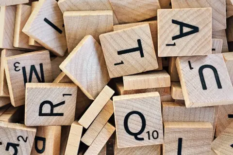 Houten lettertegels, zoals gebruikt bij moderne vreemde talen, liggen door elkaar. Letters als A, T, R, Q en N zijn zichtbaar.