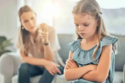 Een meisje met gekruiste armen toont duidelijk oppositioneel gedrag, terwijl haar moeder op de achtergrond met haar vinger waarschuwt.