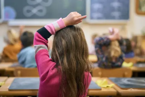 Een meisje met dyscalculie op de middelbare school steekt haar vinger op, hopend op hulp bij de sommen op het bord.