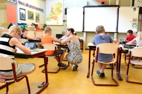 Een lerares geeft individuele aandacht aan leerlingen in een klaslokaal, wat de kern vormt van traumasensitief onderwijs.