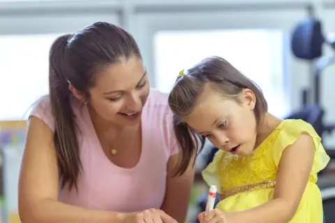 Een vrouw helpt een meisje met autisme met haar huiswerk. Ze probeert haar zin te doordrijven en te motiveren.