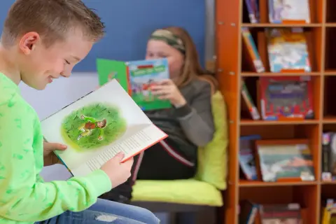 Jongen in groen shirt geniet van een boek met een illustratie. Achter hem leest een meisje. Dit is een typisch beeld van lezen groep 4.