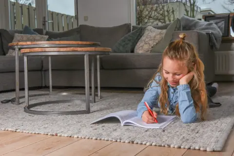 Een meisje ligt op een kleed en maakt huiswerk, ze oefent met breuken delen.