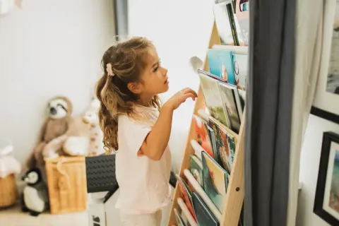 Een meisje met blond haar kijkt aandachtig naar de boekenplank, klaar om een nieuw avontuur te ontdekken. Ze houdt van lezen, kinderen.