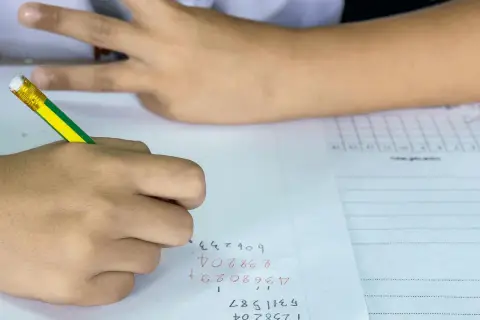 Een leerling uit groep 8 is bezig met rekenen. De leerling schrijft cijfers op papier, met een potlood.