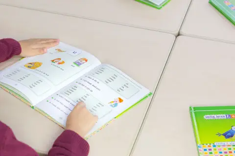 Meisje leest in een boek om technisch lezen te verbeteren. Woorden en zinnen helpen haar met oefenen.