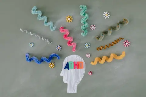 Kleurrijke linten en bloemen omringen een hoofdprofiel met de letters "ADHD". Dit symboliseert de zoektocht naar een kind behandeling.